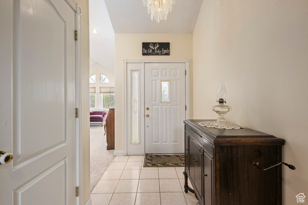 Entrance foyer with light colored carpet, baseboards, light tile patterned flooring, and a notable chandelier