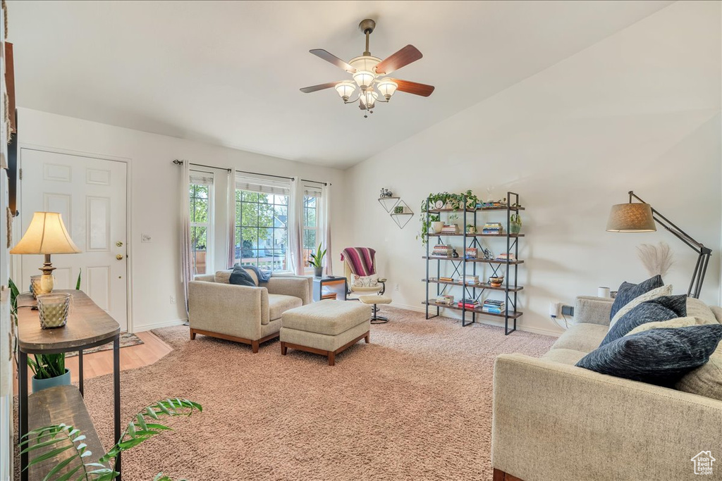 Living room with baseboards, ceiling fan, vaulted ceiling, and light carpet