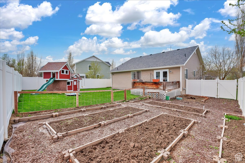 Rear view of property with a fenced backyard, a playground, a yard, and a vegetable garden