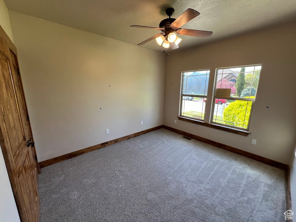 Spare room with a textured ceiling, ceiling fan, light colored carpet, and baseboards