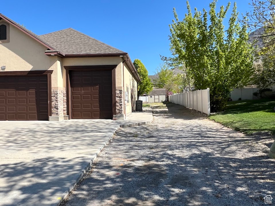 View of property exterior featuring a garage, fence, stone siding, stucco siding, and driveway