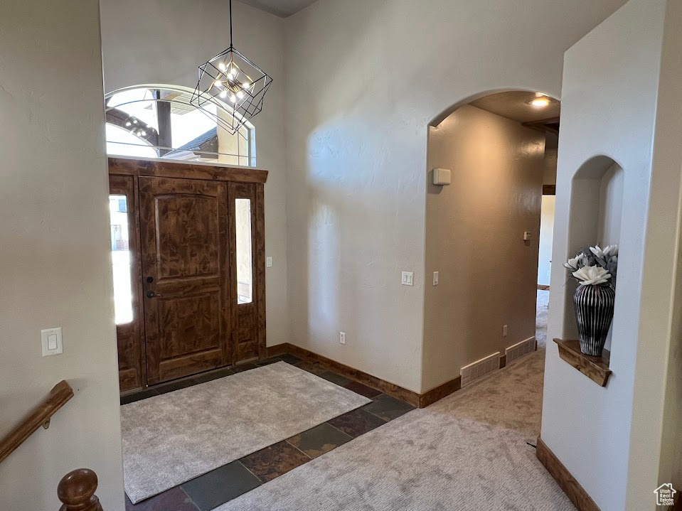 Carpeted entrance foyer with baseboards, arched walkways, and an inviting chandelier