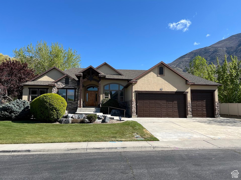 View of front facade featuring stone siding, a garage, stucco siding, a front yard, and concrete driveway