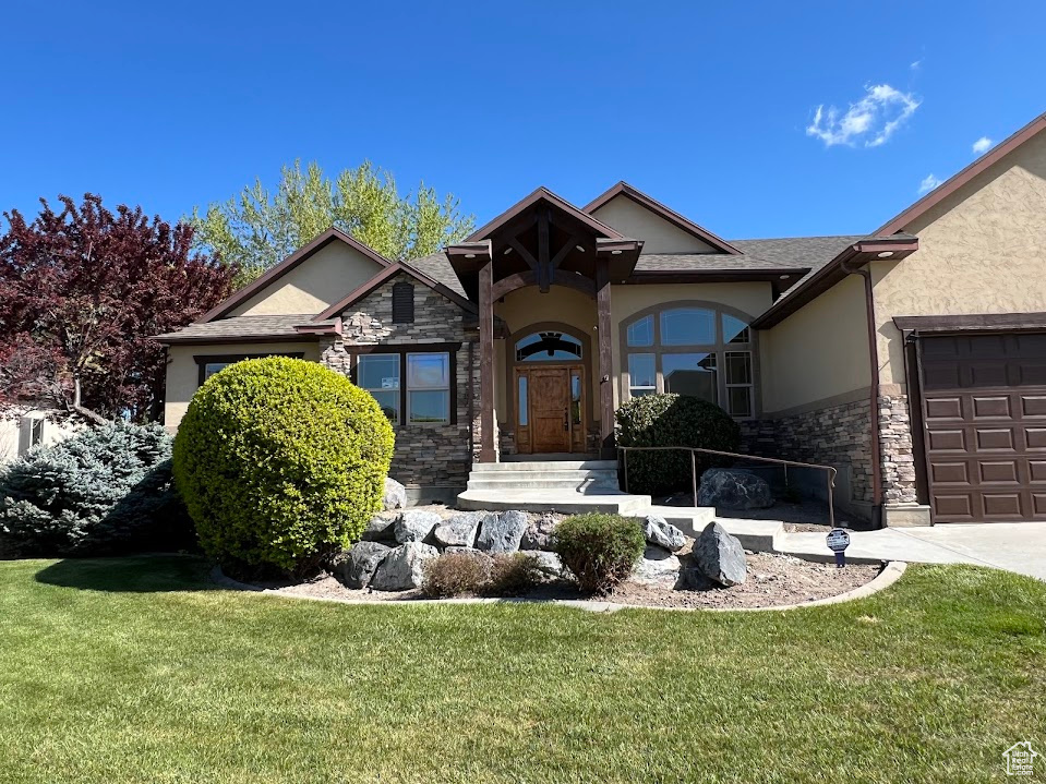 View of front of property featuring stucco siding, a front yard, and stone siding