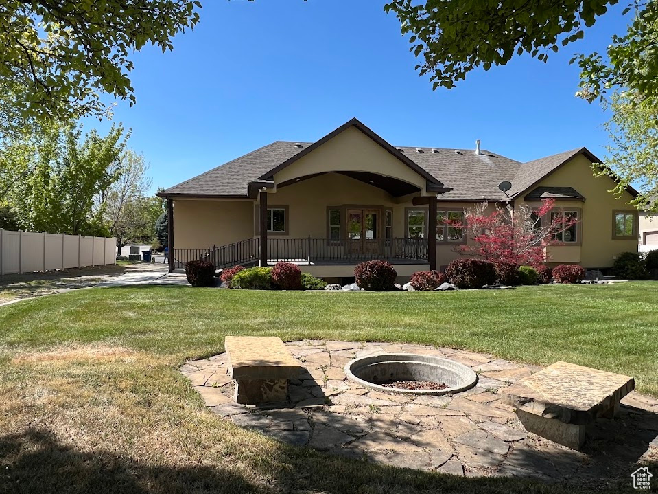 Back of property with fence, roof with shingles, stucco siding, a lawn, and an outdoor fire pit