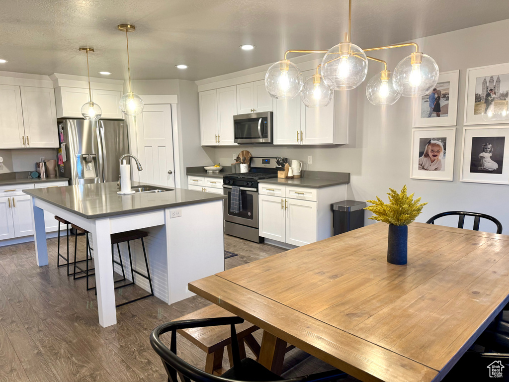 Kitchen with dark wood-style flooring, dark countertops, appliances with stainless steel finishes, a breakfast bar, and a sink