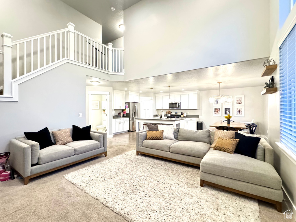 Living area featuring light colored carpet, a towering ceiling, and stairway