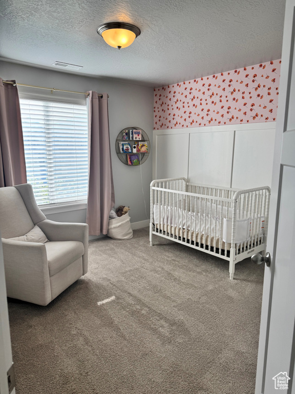 Carpeted bedroom featuring a crib, wainscoting, a textured ceiling, and visible vents