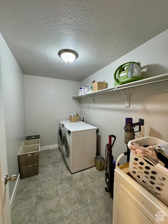 Washroom featuring laundry area, baseboards, a textured ceiling, and washing machine and dryer