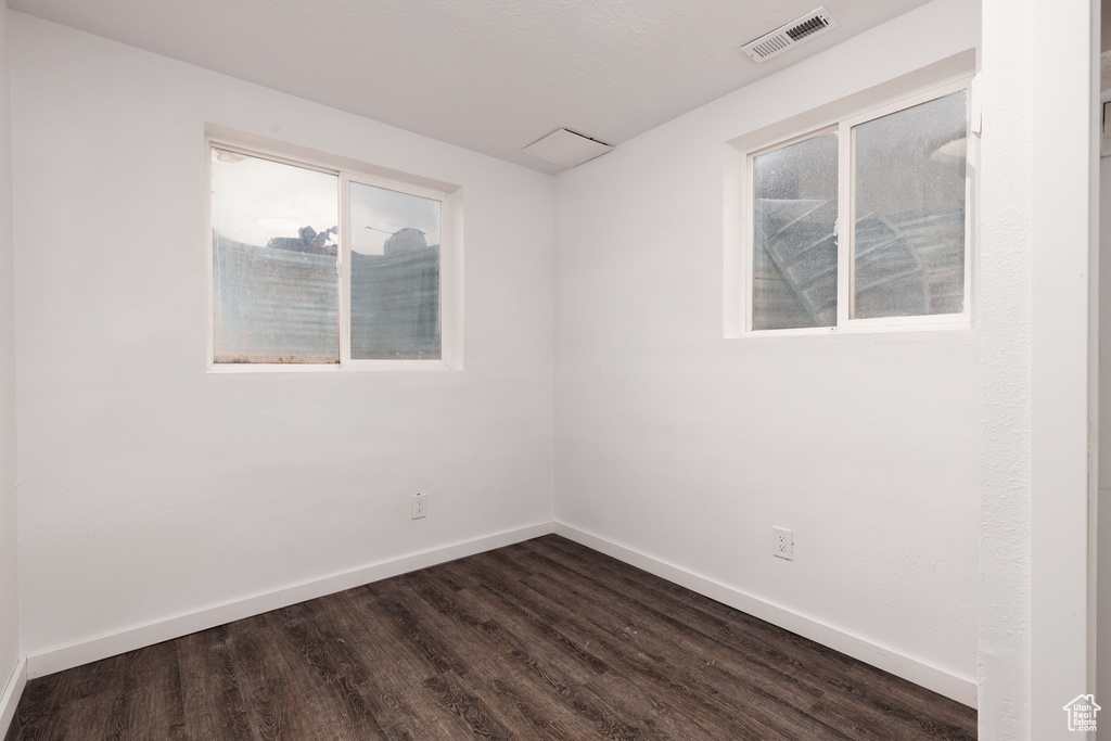 Empty room featuring baseboards, visible vents, dark wood-style floors, and a wealth of natural light