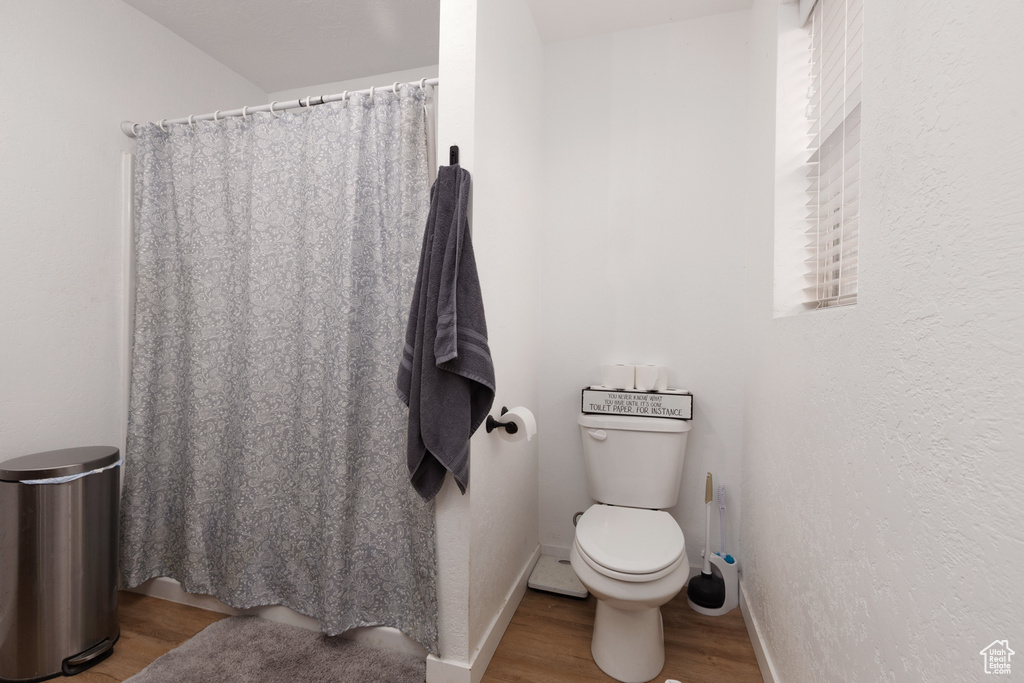 Bathroom featuring toilet, baseboards, curtained shower, and wood finished floors