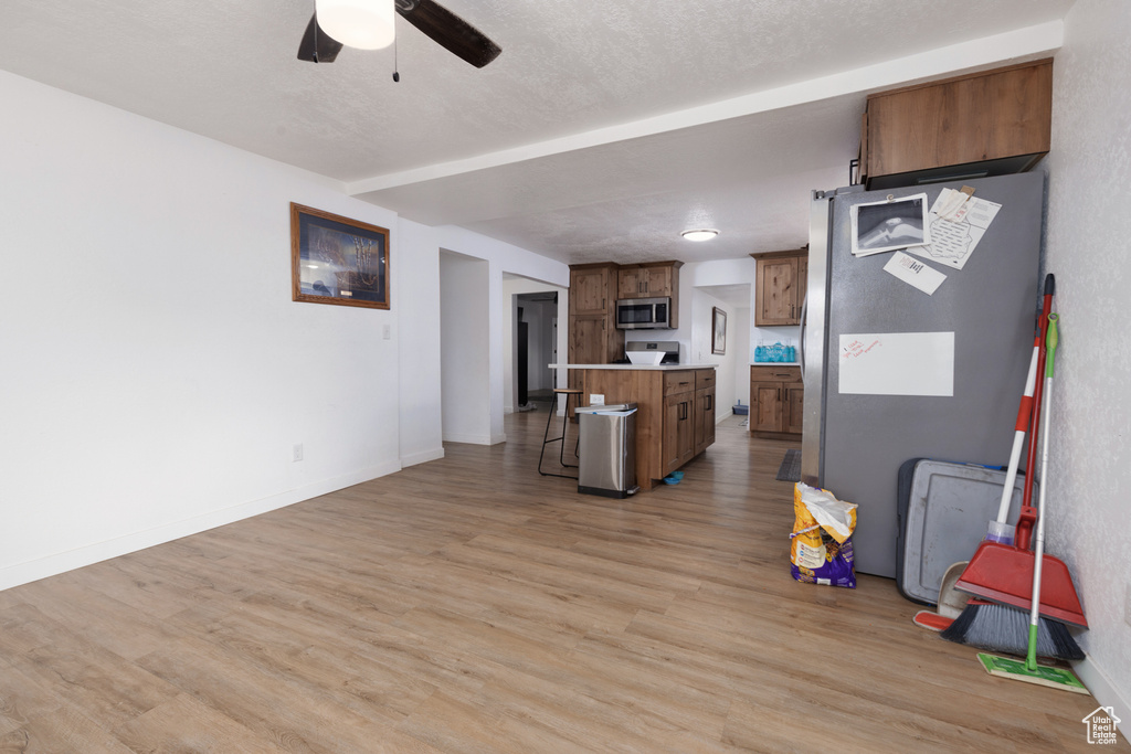 Interior space with a breakfast bar area, a kitchen island, brown cabinets, stainless steel microwave, and light wood-style floors