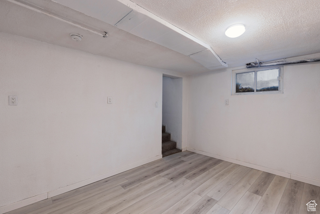 Below grade area featuring baseboards, light wood-type flooring, a textured ceiling, and stairs