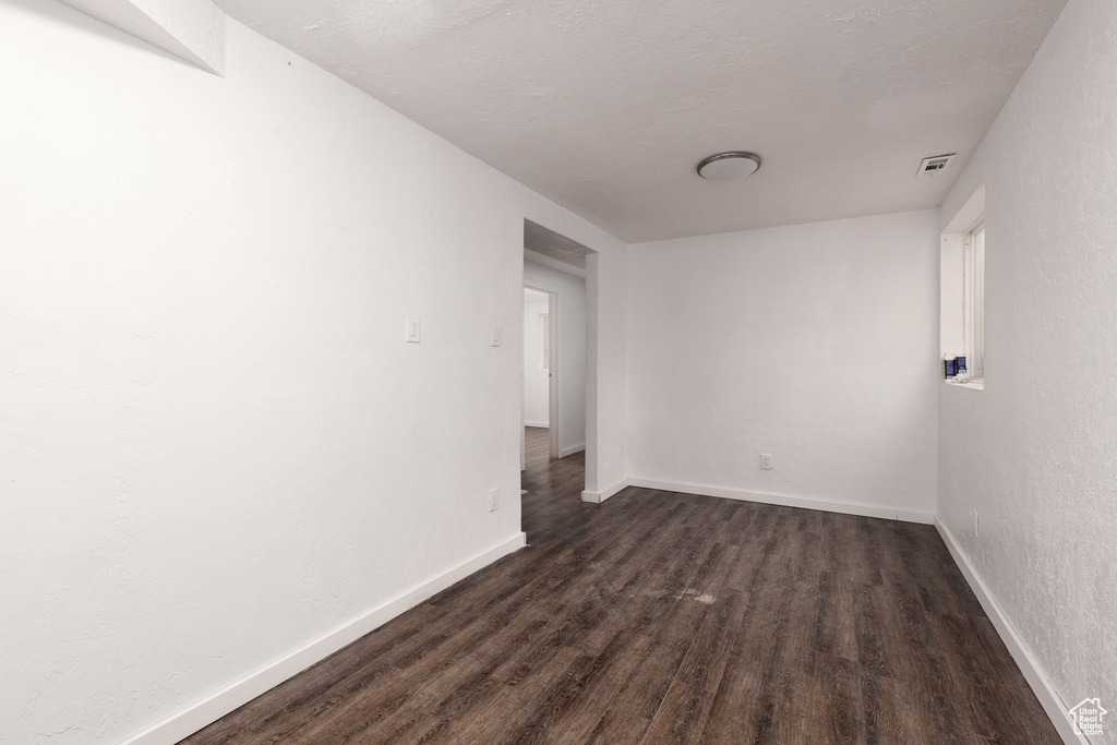 Spare room with visible vents, baseboards, and dark wood-style floors