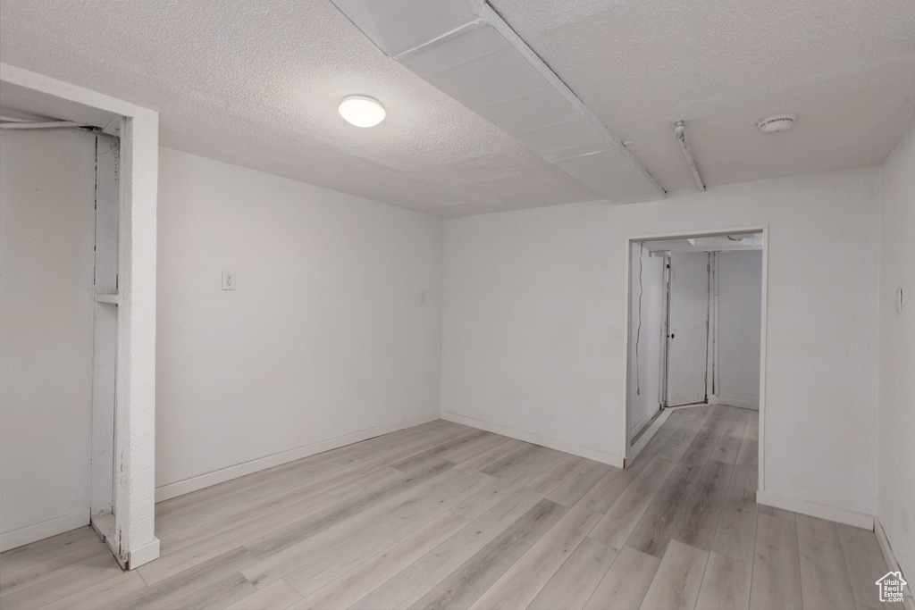 Below grade area featuring baseboards, light wood-type flooring, and a textured ceiling