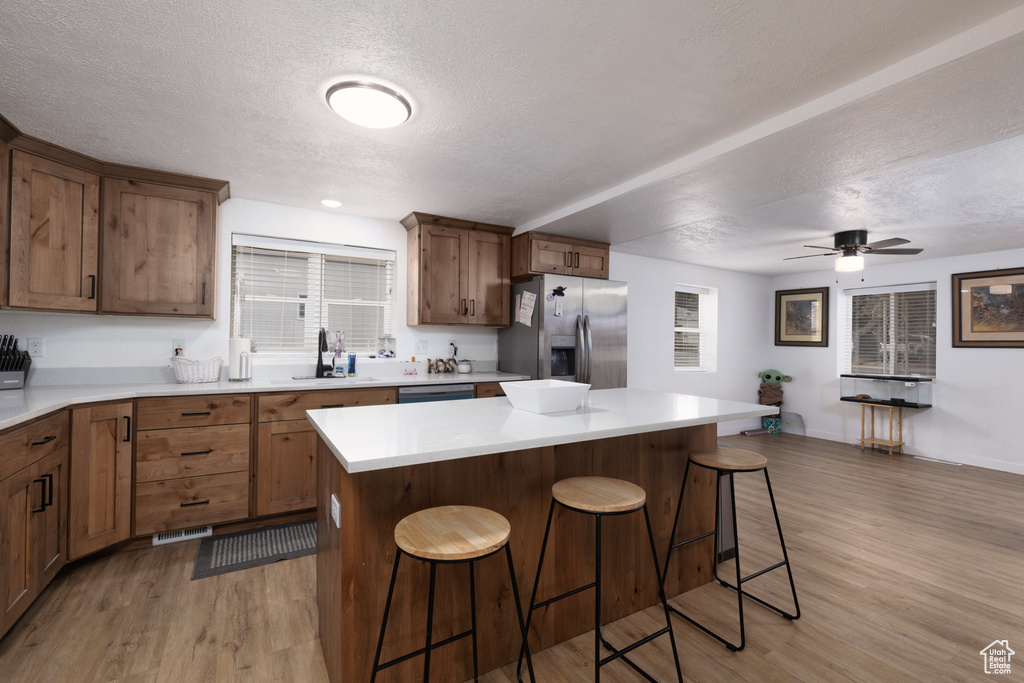 Kitchen with a textured ceiling, stainless steel fridge, light wood-style flooring, and a kitchen bar