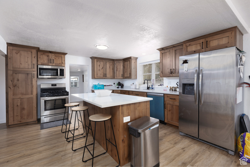 Kitchen featuring stainless steel appliances, a textured ceiling, a center island, and light wood-style floors