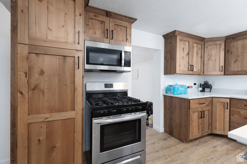Kitchen featuring brown cabinetry, a textured ceiling, light countertops, light wood-style floors, and stainless steel appliances