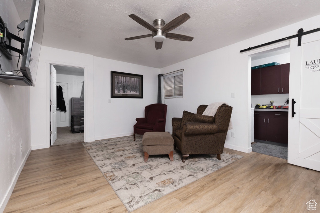 Living area with a ceiling fan, a textured ceiling, light wood-type flooring, a barn door, and baseboards