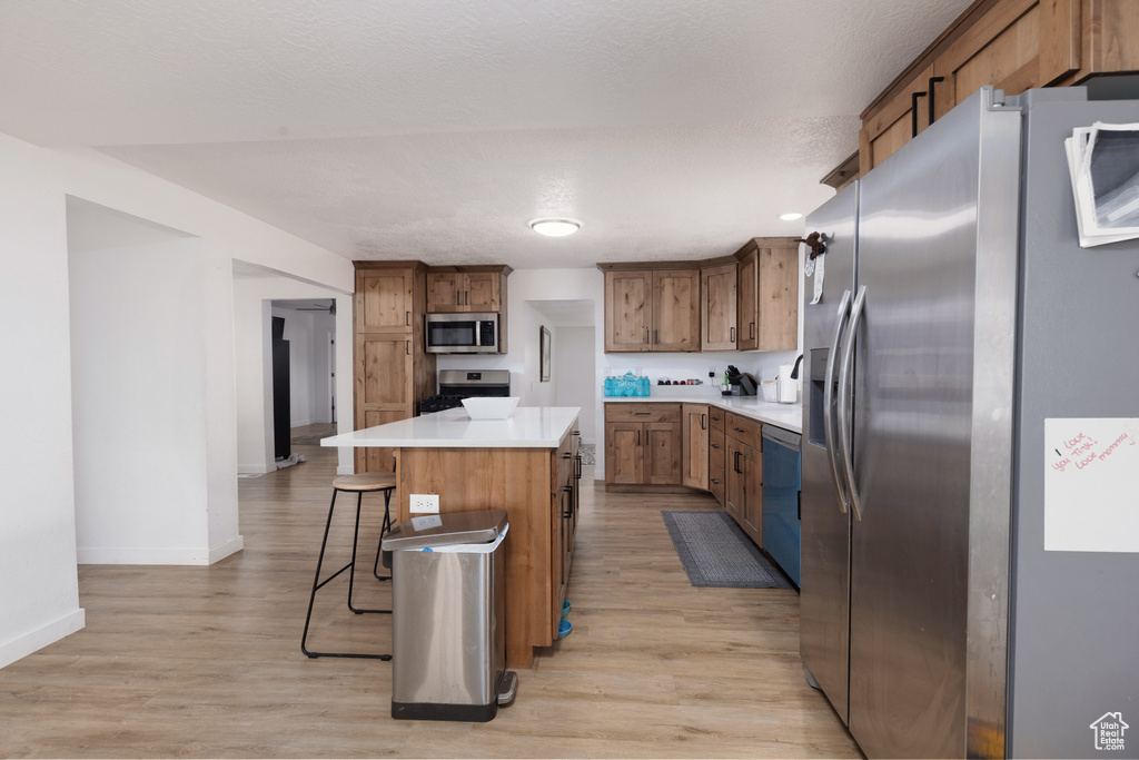 Kitchen with baseboards, a kitchen breakfast bar, a center island, light wood finished floors, and stainless steel appliances