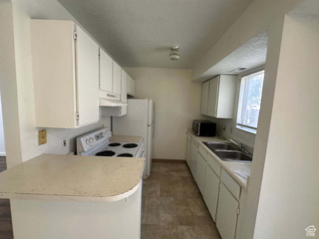 Kitchen with light countertops, stainless steel microwave, under cabinet range hood, white range with electric stovetop, and a sink