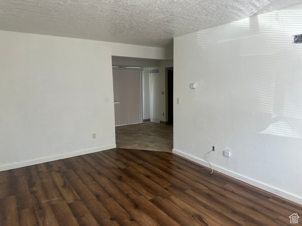 Spare room with baseboards, dark wood-style floors, a textured ceiling, and visible vents