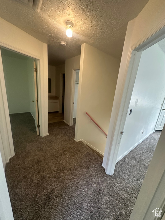 Hallway with carpet, a textured ceiling, and an upstairs landing