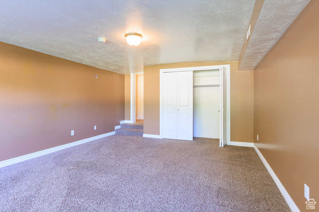 Unfurnished bedroom featuring a textured ceiling, baseboards, carpet, and a closet