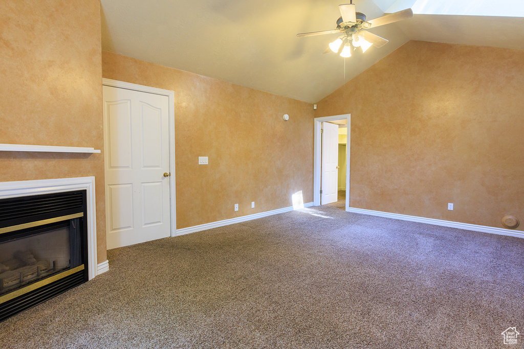 Unfurnished living room featuring carpet floors, a ceiling fan, a glass covered fireplace, and vaulted ceiling