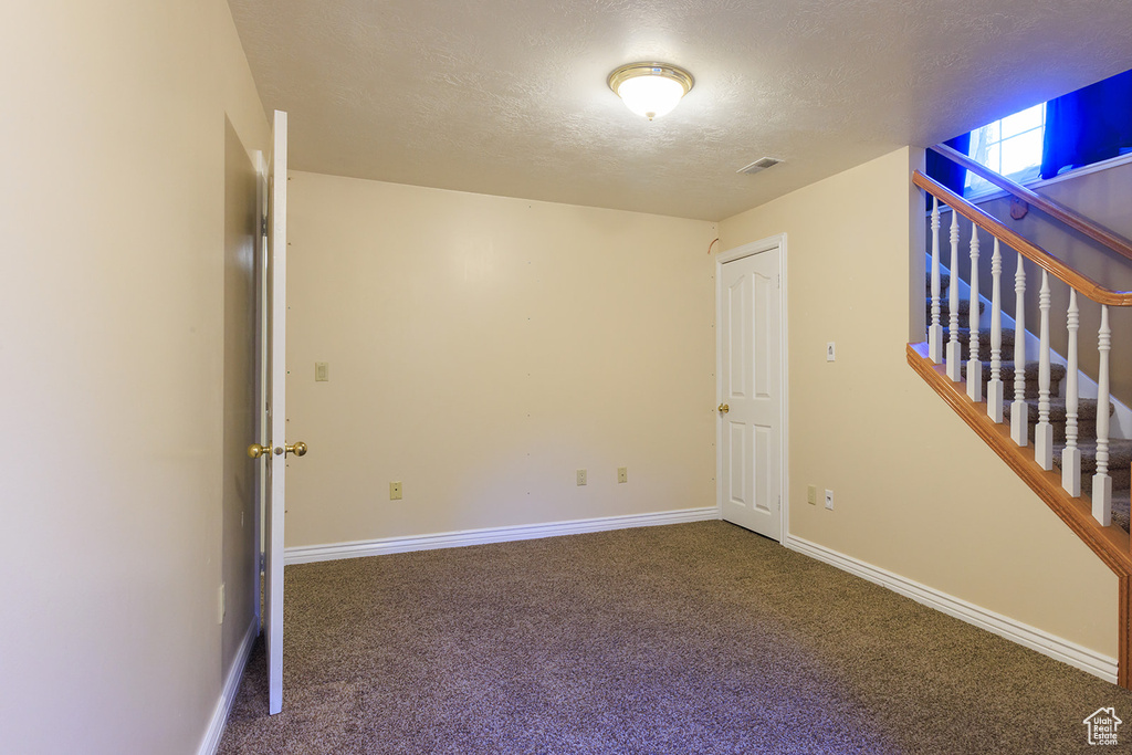 Empty room featuring a textured ceiling, visible vents, baseboards, carpet flooring, and stairs