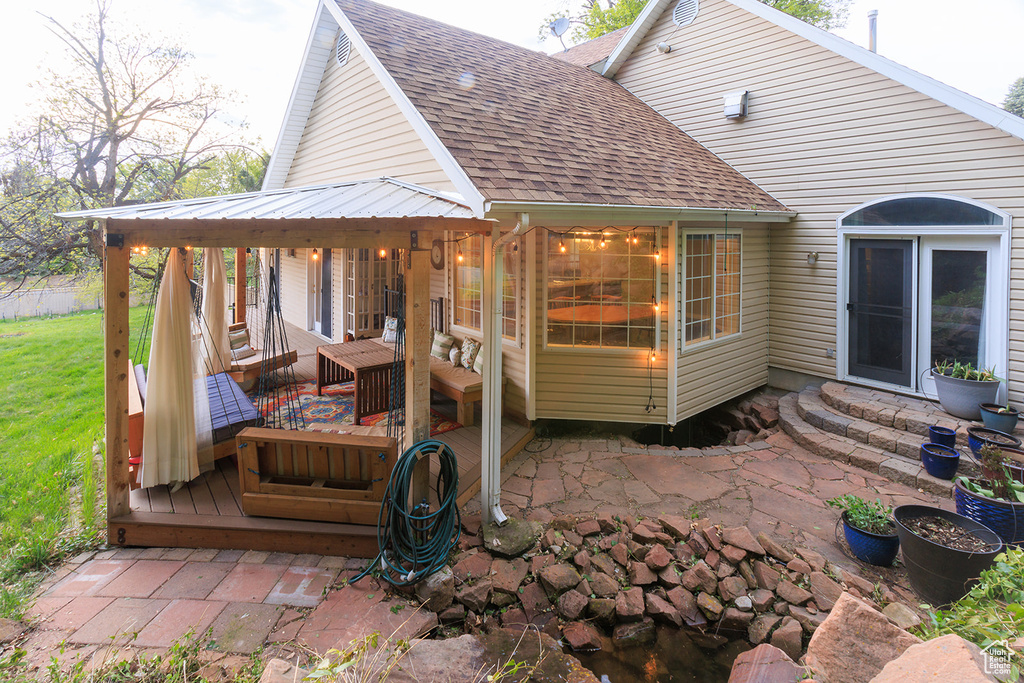 Exterior space with a shingled roof, a patio area, a wooden deck, and entry steps