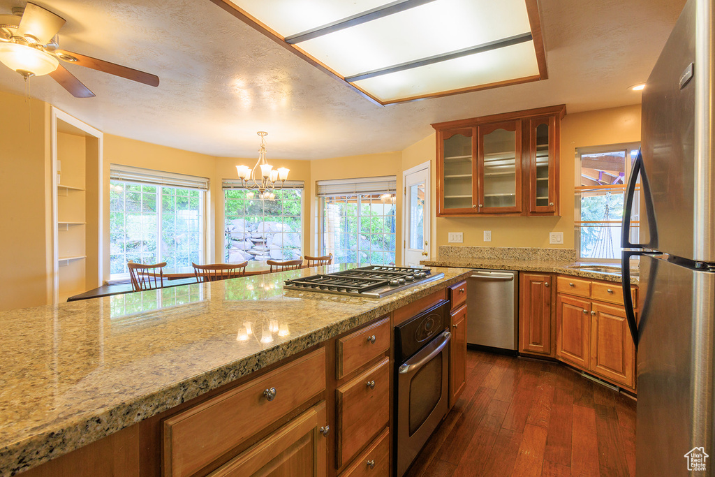 Kitchen featuring brown cabinets, light stone countertops, stainless steel appliances, dark wood-type flooring, and glass insert cabinets