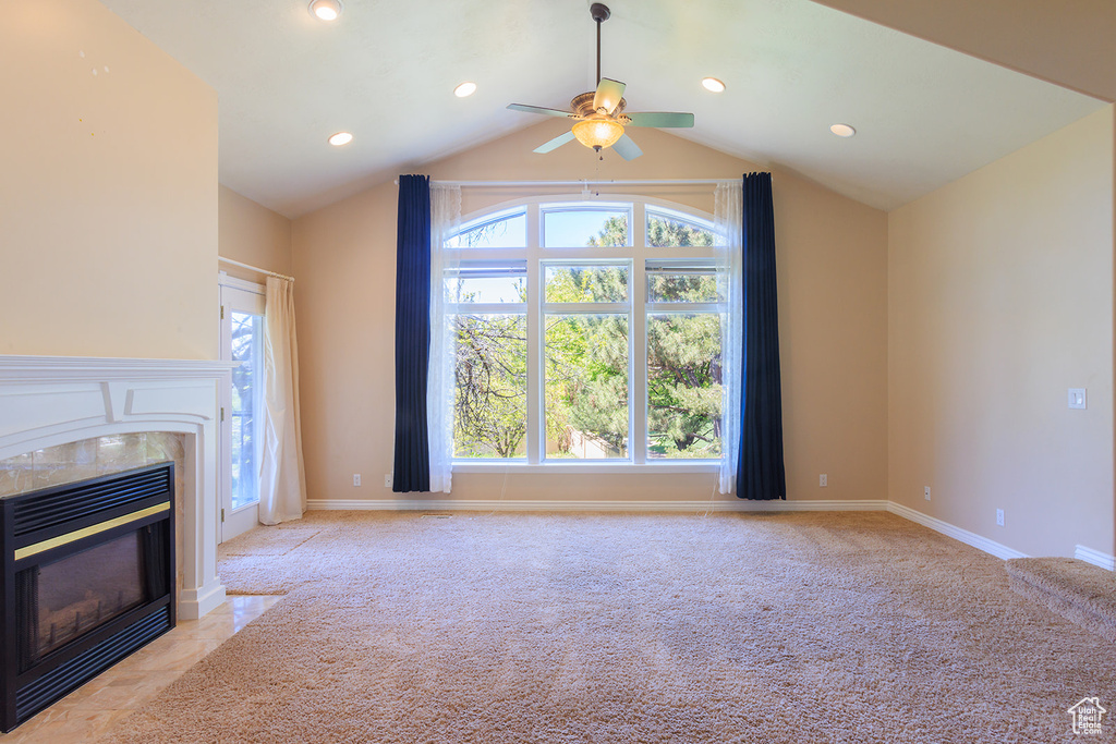 Unfurnished living room with ceiling fan, vaulted ceiling, a wealth of natural light, and a fireplace