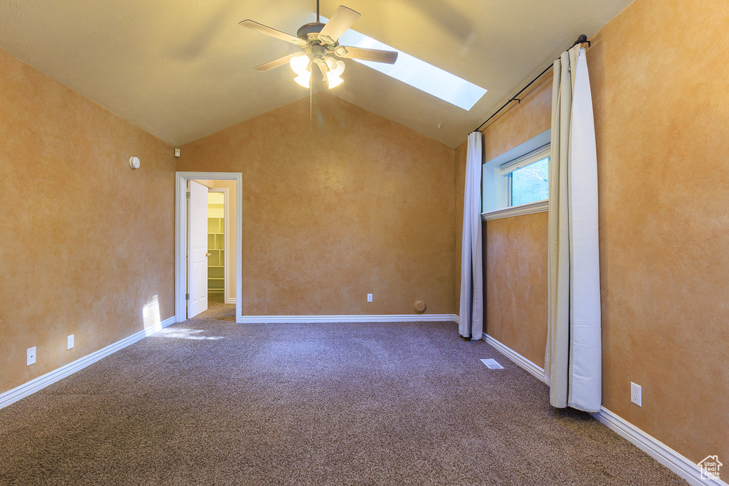 Carpeted empty room with ceiling fan, lofted ceiling with skylight, and visible vents