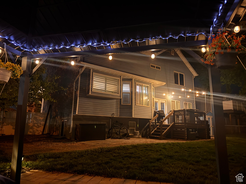 Back of house at night featuring a lawn, stairs, and a wooden deck