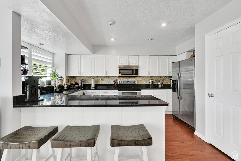 Kitchen featuring stainless steel appliances, a textured ceiling, tasteful backsplash, and a peninsula