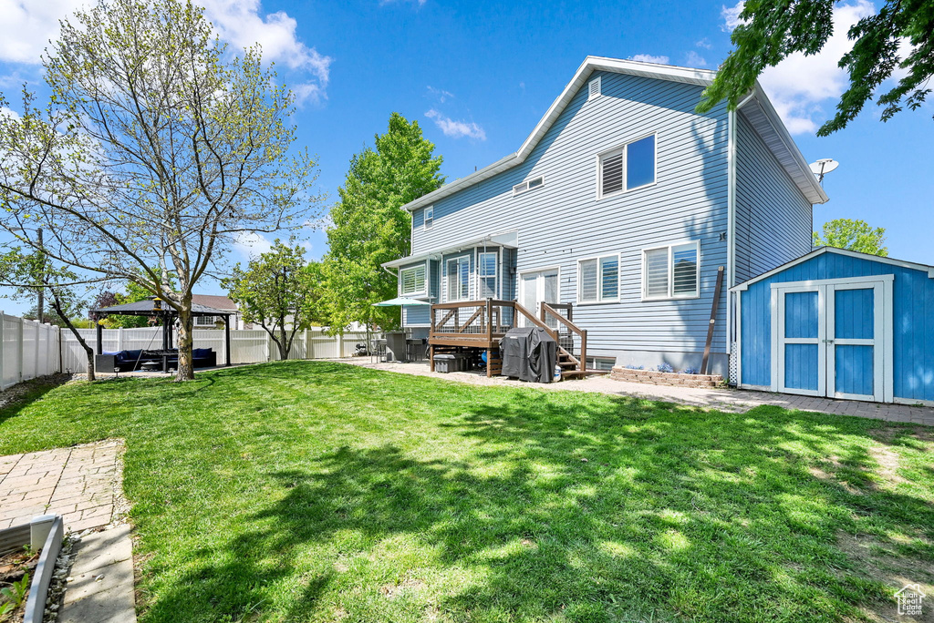 Rear view of house with a fenced backyard, a storage unit, an outbuilding, a patio area, and a yard