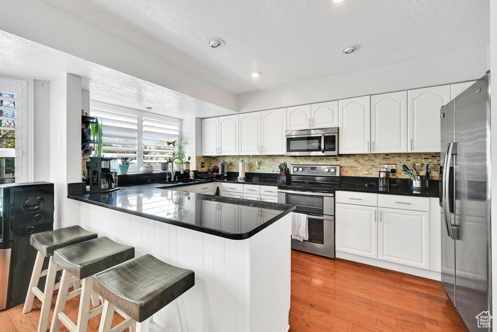 Kitchen featuring a peninsula, dark countertops, a textured ceiling, white cabinetry, and stainless steel appliances