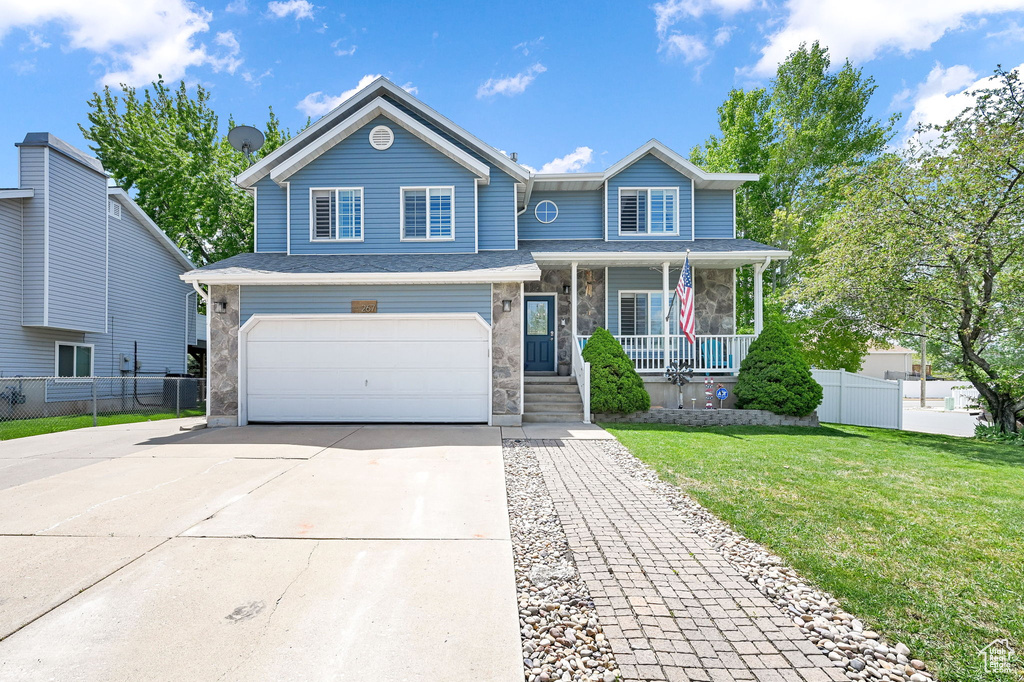 Traditional-style home with a front lawn, an attached garage, fence, a porch, and driveway