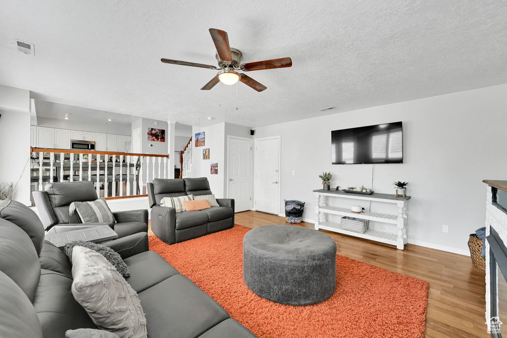 Living room featuring a ceiling fan, a textured ceiling, a fireplace, light wood finished floors, and stairs