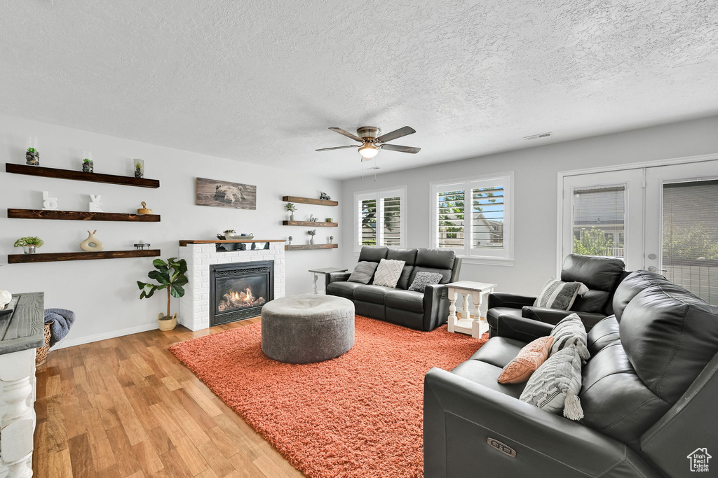 Living room featuring a textured ceiling, ceiling fan, visible vents, and light wood-style floors