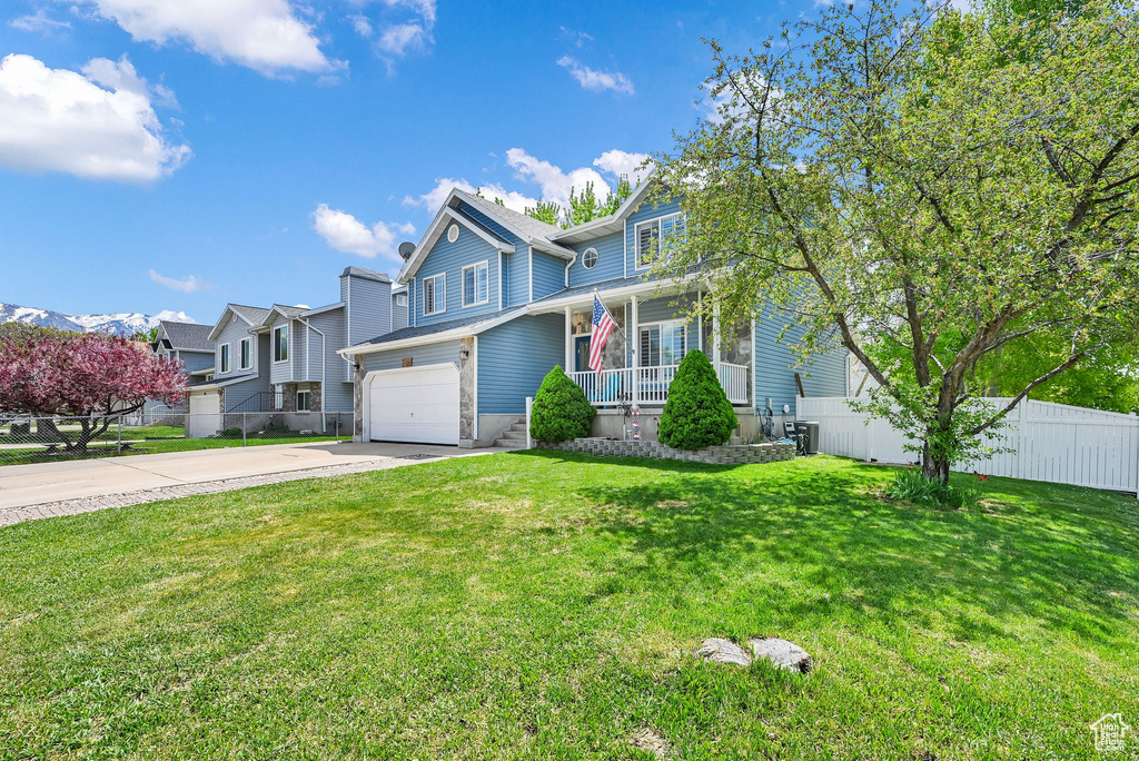 View of front facade featuring fence, an attached garage, a front lawn, a porch, and driveway