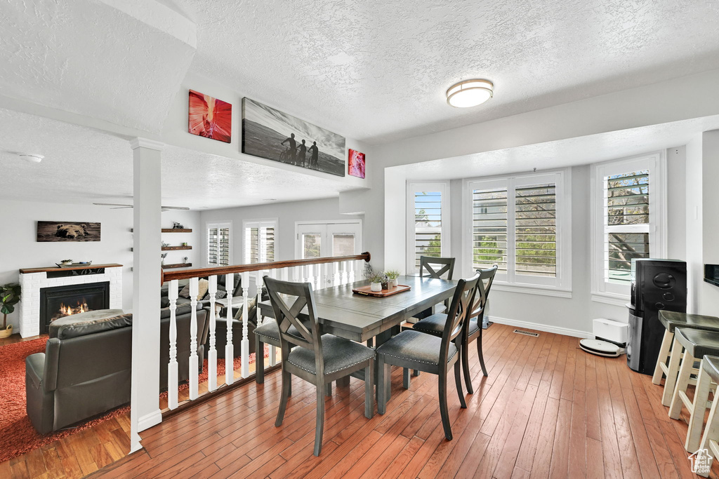 Dining area with a warm lit fireplace, a textured ceiling, and light wood-style flooring