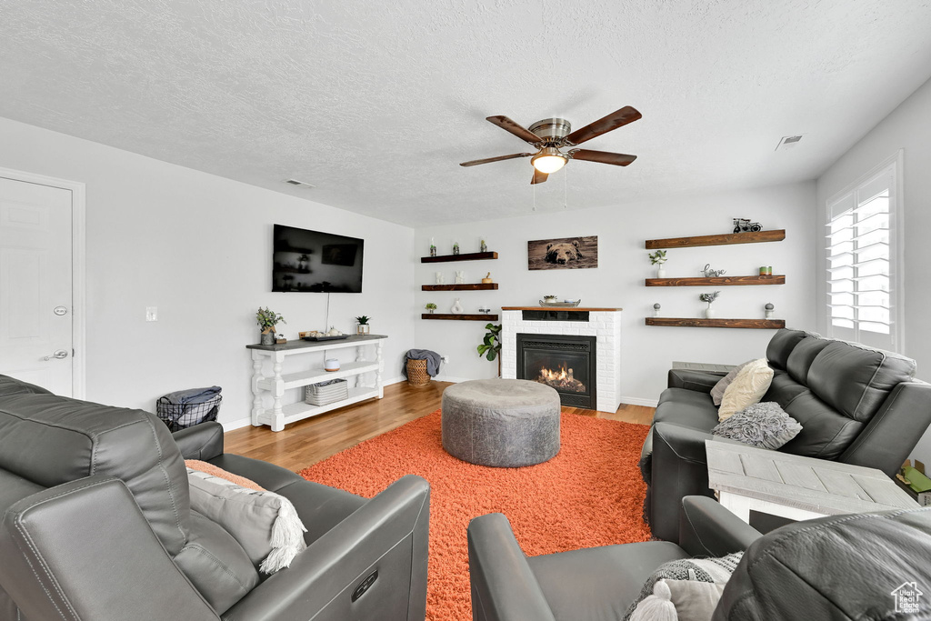 Living area with visible vents, a textured ceiling, a ceiling fan, wood finished floors, and a lit fireplace