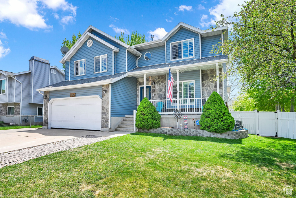 Traditional-style home with fence, an attached garage, a front lawn, covered porch, and driveway
