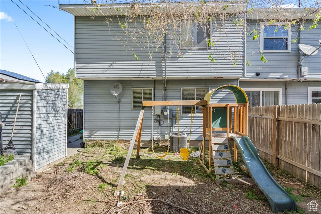 Rear view of house with central air condition unit, fence, and a playground