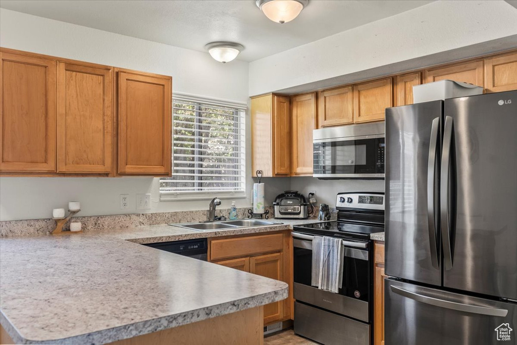 Kitchen featuring a peninsula, light countertops, brown cabinets, a sink, and stainless steel appliances