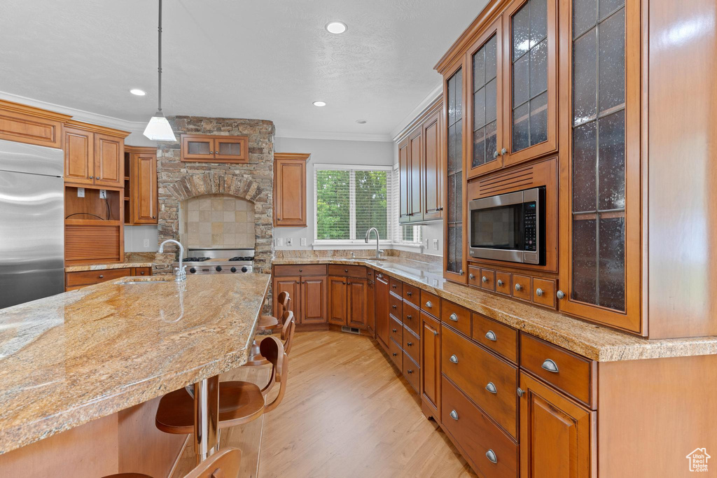 Kitchen with a sink, built in appliances, a kitchen breakfast bar, and light wood-style floors