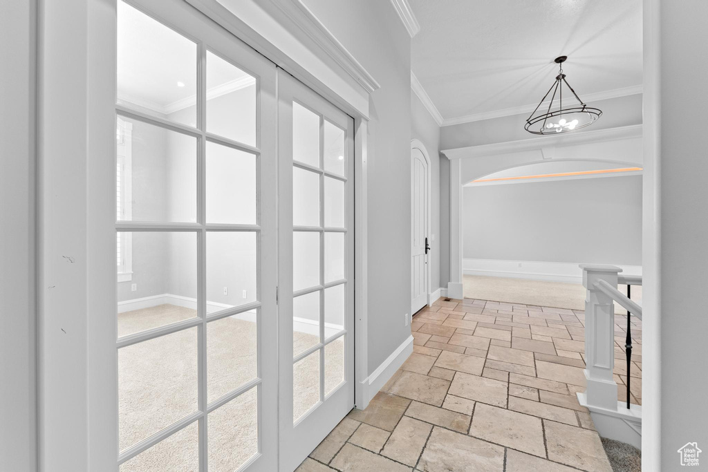 Corridor with an inviting chandelier, baseboards, ornamental molding, and stone tile floors