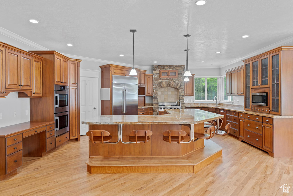 Kitchen featuring crown molding, built in appliances, brown cabinets, a large island with sink, and a sink